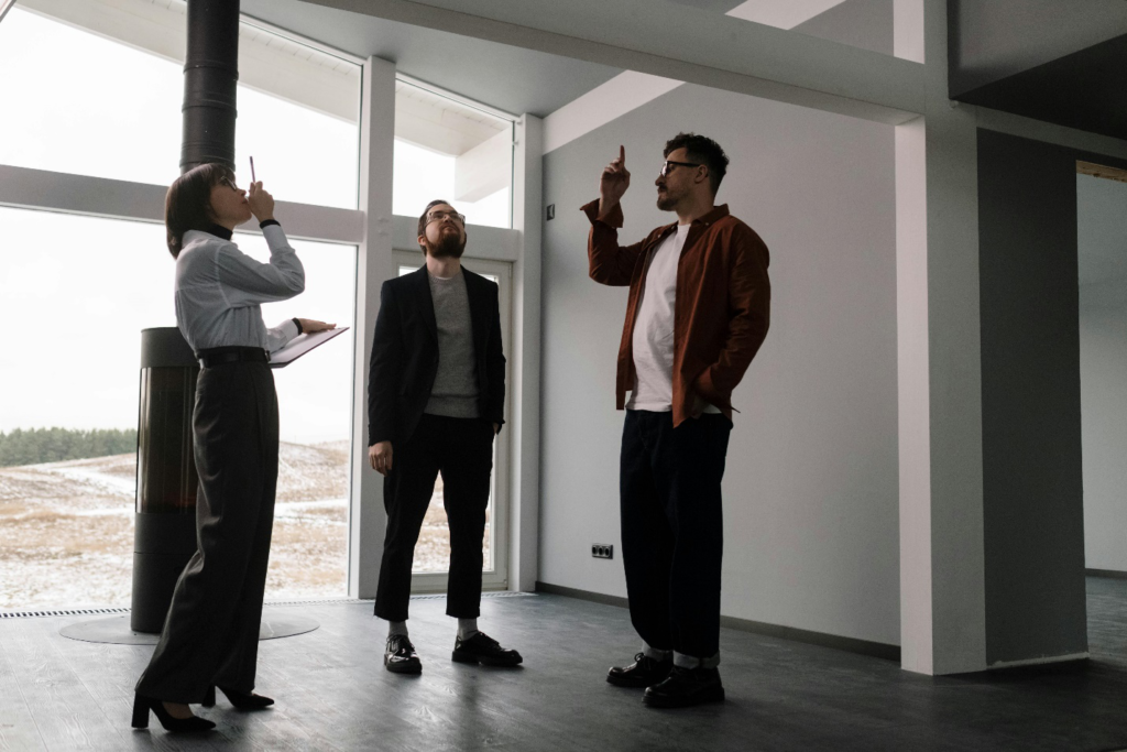 Three people inspecting a modern home interior, examining the ceiling, and discussing details during a property tour
