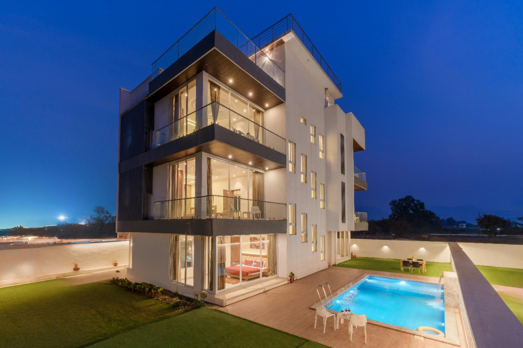 A luxurious three-story modern home with floor-to-ceiling glass windows, featuring a private swimming pool
