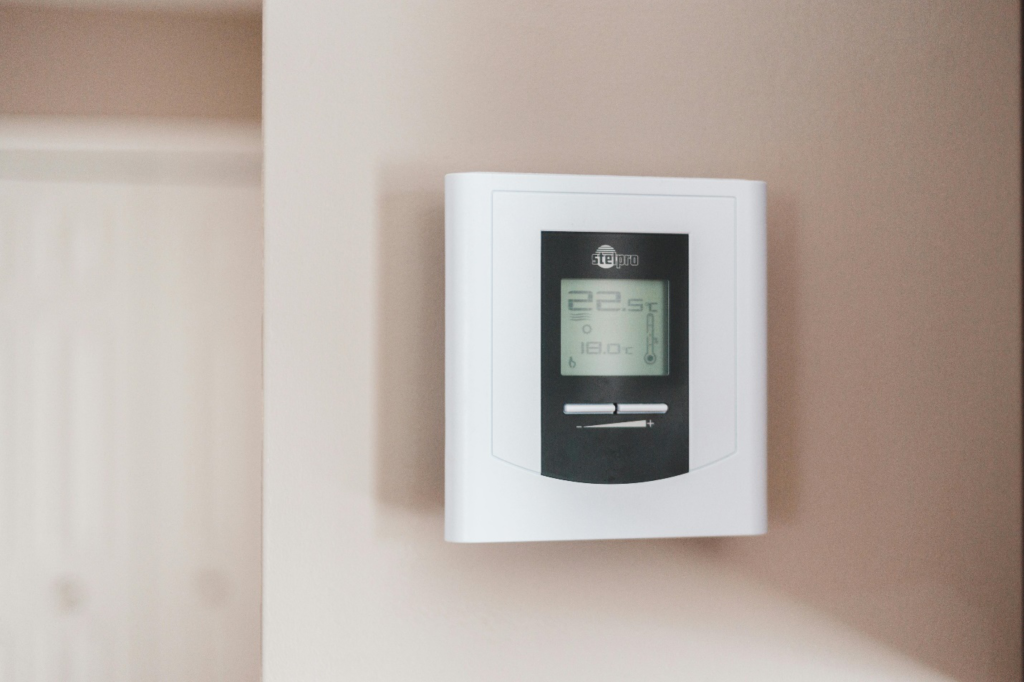 Modern digital thermostat mounted on a beige wall, displaying temperature settings 